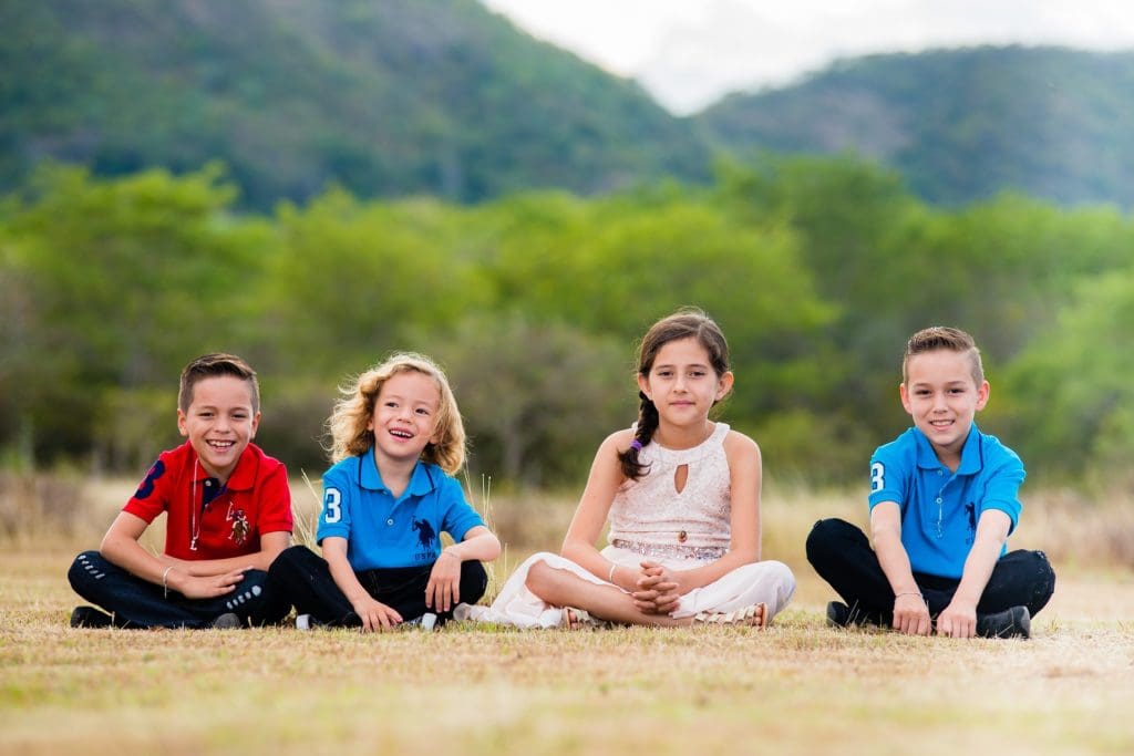 Four children sitting outside, smiling and posing for the camera.