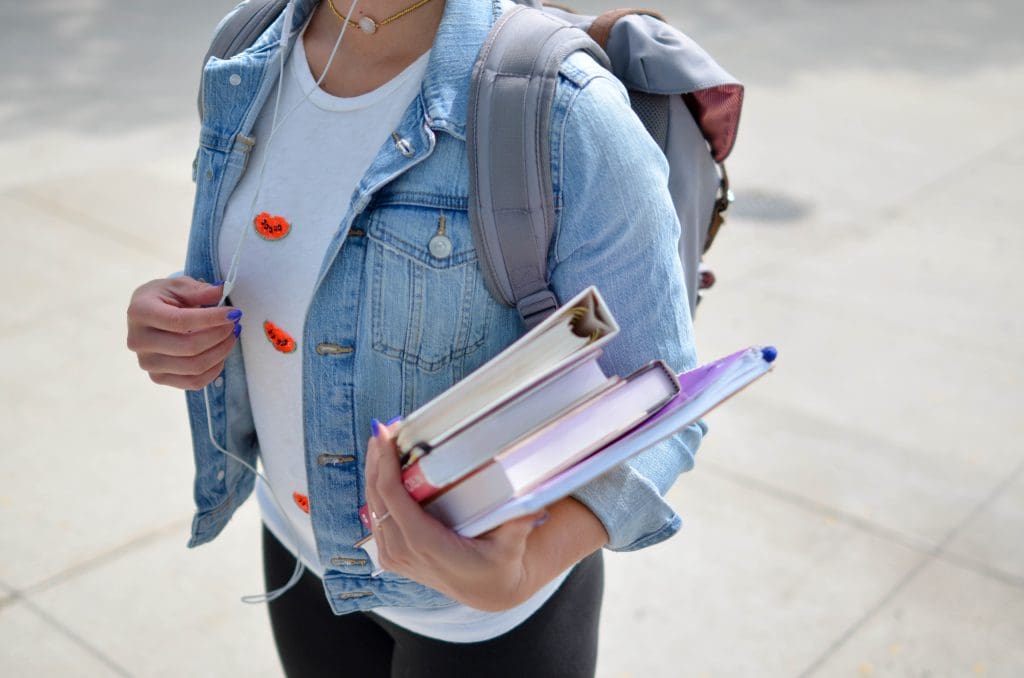 A student with a backpack holding a pile of books.