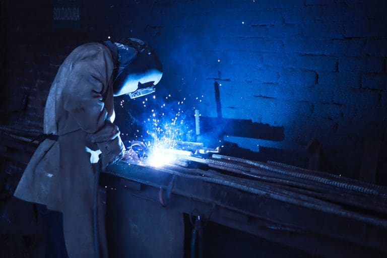 A person welding metal. They are wearing a welding helmet and no part of their face is visible.